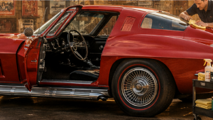 Red classic Corvette coupe with the driver door open while a detailer wipes the roof beside a product cart